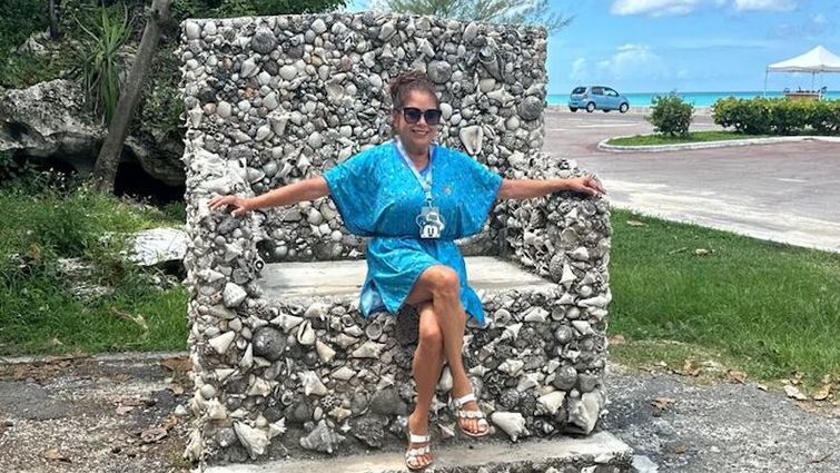 Brenda Roper sits on cobblestone throne or chair in a blue dress and sunglasses
