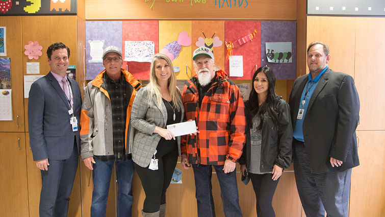 two male hospital administrators, one female Children's Hospital foundation representative, and three people from Quaid Harley-Davidson pose for photo with check