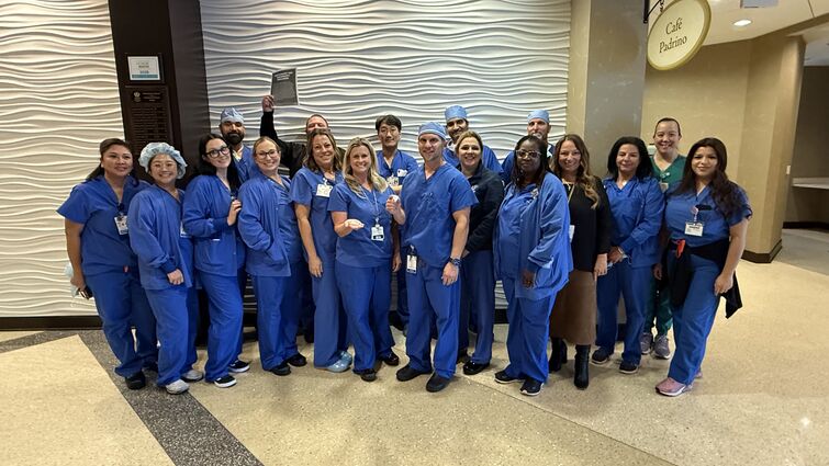 A large group of people in medical scrubs posing together in a hospital lobby.