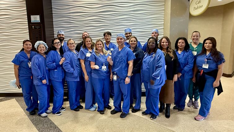 A large group of people in medical scrubs posing together in a hospital lobby.