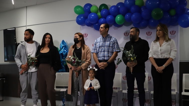 Six people stand shoulder to shoulder in front of blue and green balloon backdrop.