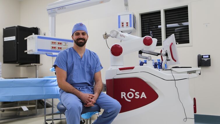 Doctor in blue scrubs sitting in front of a Rosa robot 