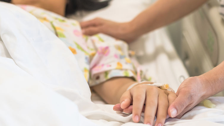 Nursing caretaker concept with kid patient sleeping in bed with family caregiver hand support in blur medical hospital background (focus on hand)