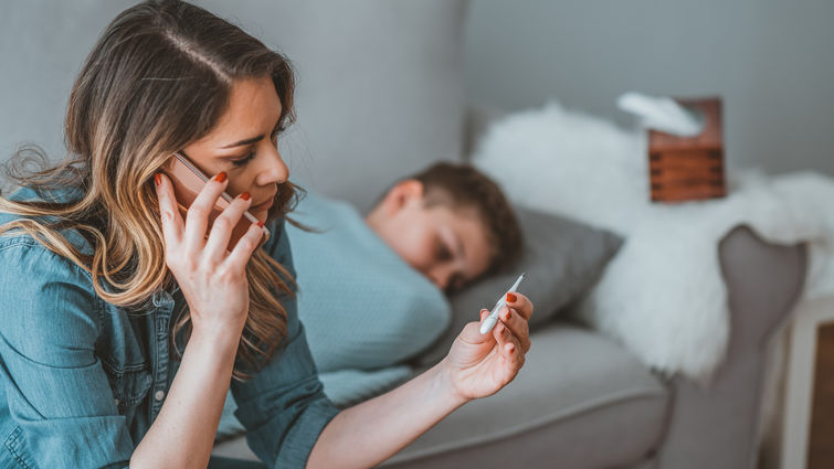 worried mother taking temperature of her little son who is lying in bed with fever