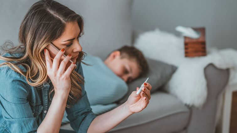 worried mother taking temperature of her little son who is lying in bed with fever