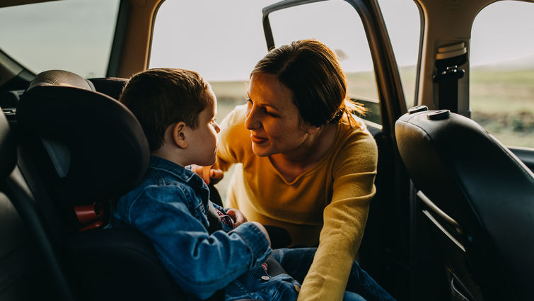 Mother talking to son in back of the car as she fixes car seat