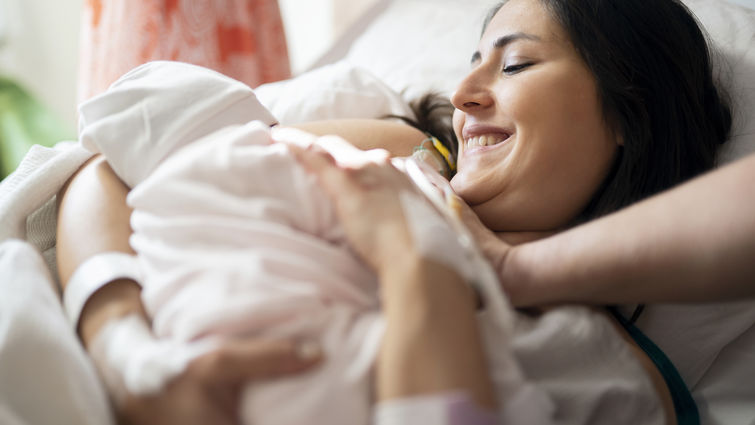 Mother breastfeeding newborn baby in hospital ward, first breastfeeding