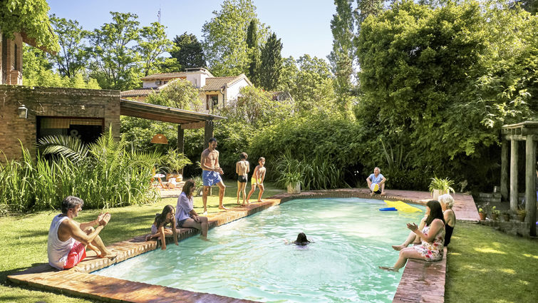 Wide angle view of multi-generation family relaxing and watching children play and swim in backyard pool