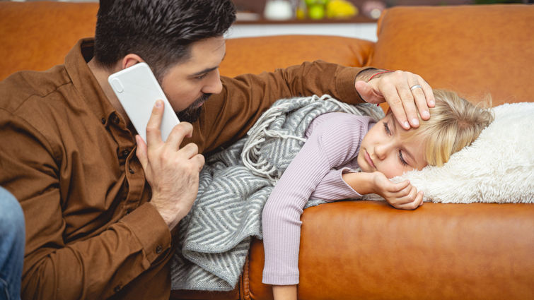 Caring father calling doctor and touching daughter forehead