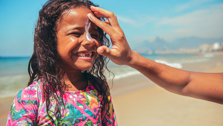 Little surfer girl preparing for surf with suntan lotion on a face