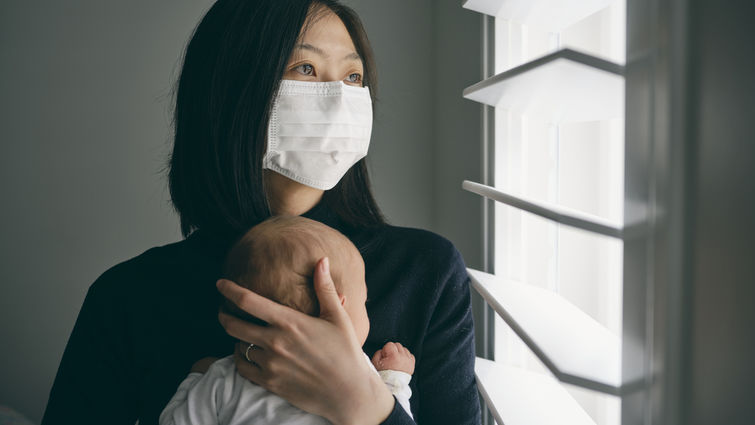 A mother wearing mask and holding baby in home isolation from infectious disease