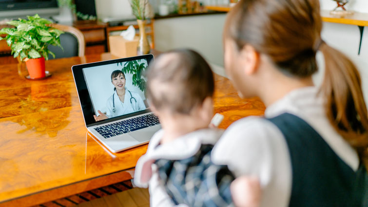 A mother with her baby is video calling a doctor on a laptop from home