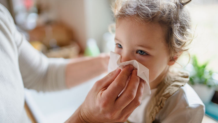 Unrecognizable father with small sick toddler daughter indoors at home, blowing nose.