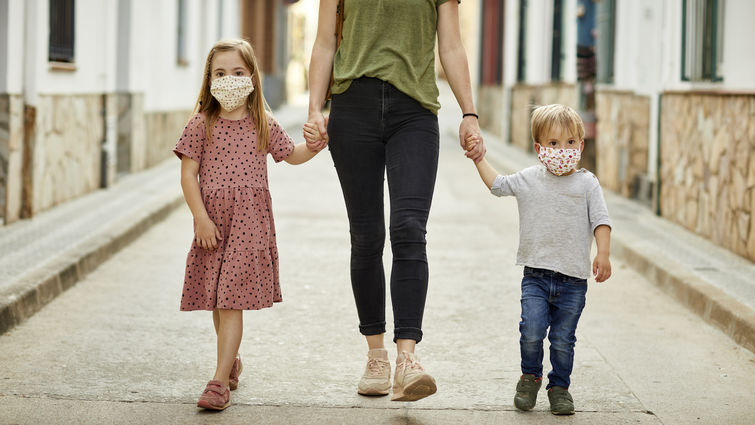 Mother with daughter and son, holding hands walking on the street, wearing home made face mask for coronavirus pandemic.