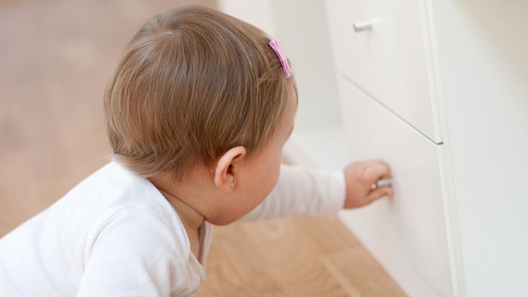 Baby girl opening a drawer with curiosity. Risks at home with little children.
