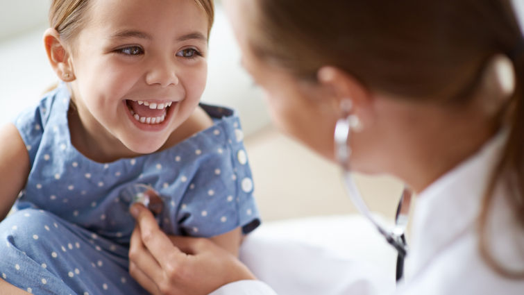 young female doctor listening to heart of young smiling girl