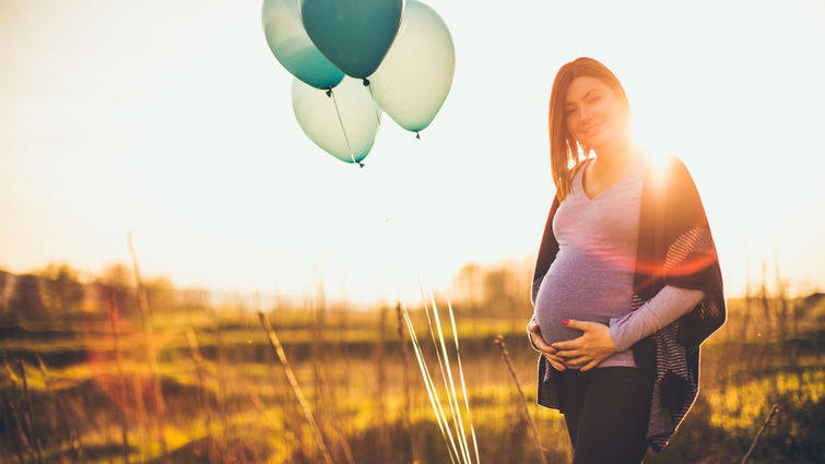 Pregnant woman standing in the middle of a field with balloons.