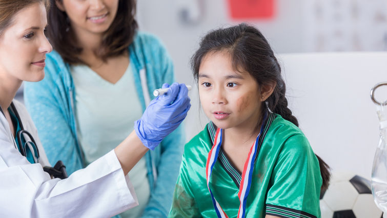 Young girl at the doctor's office with her mother. Doctor is examining her eyes following a hit.