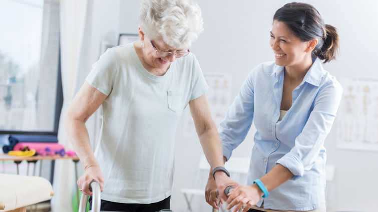 Older woman standing with walker with help from another woman