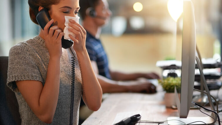 Female sneezing into napkin at her desk.