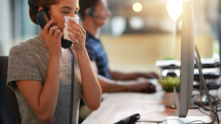 Female sneezing into napkin at her desk.