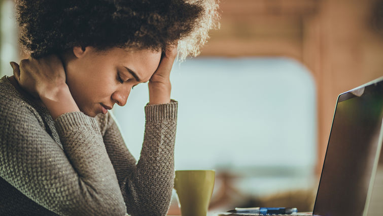 women rubbing her head while sitting in front of a computer screen