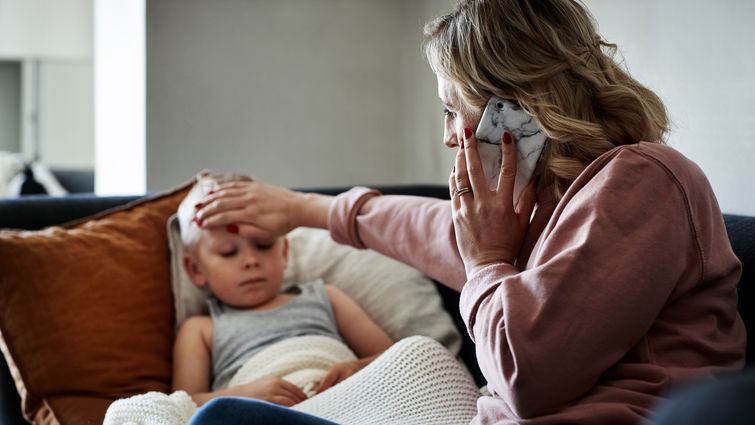 hot of a mother wearing a surgical mask making a phone call while aiding to her sick young son at home