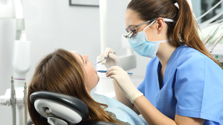 Female dentist cleans the teeth of a female patient in a dental office.
