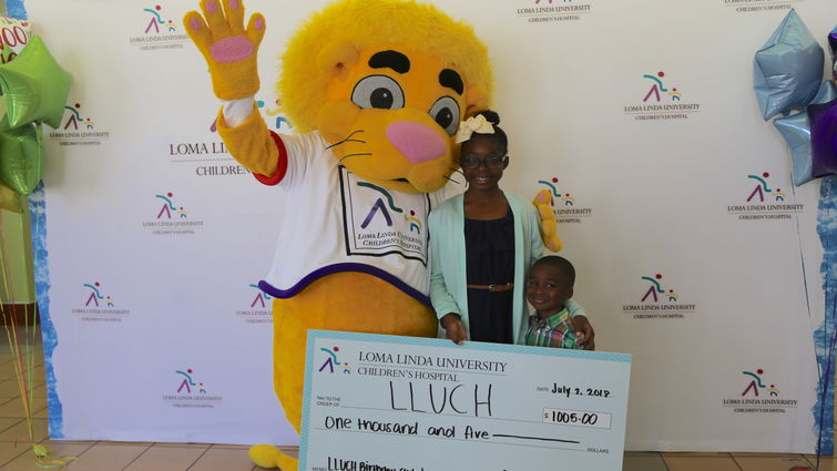 Mascot, Alyssa Jean-Marie, and Ashton hold the donation check