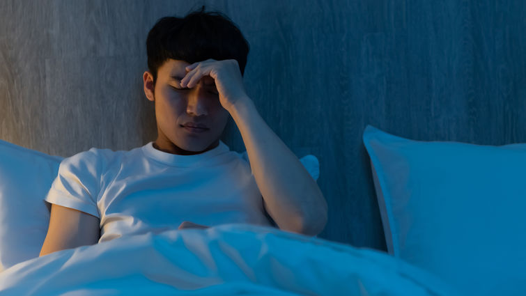 Young male sitting up in bed pinching his head as if in pain