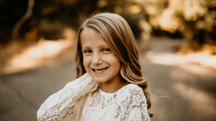 young blond girl smiling widely at the camera in outdoor photo