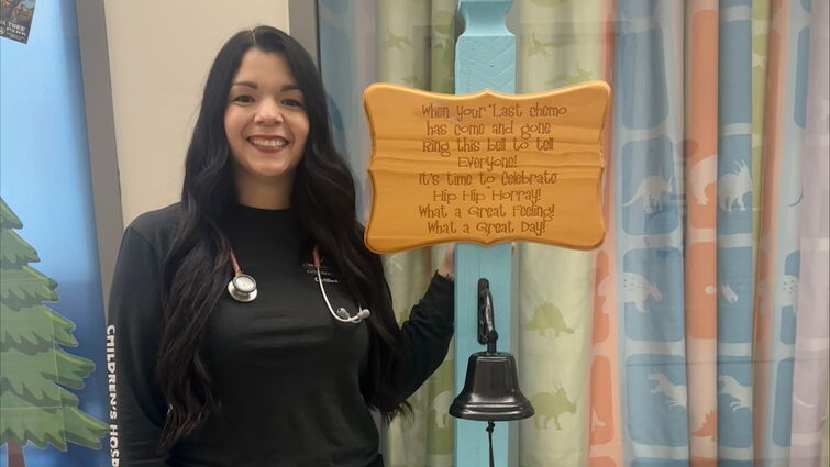 Heather Kono stands by cancer free bell on pediatric cacner unit