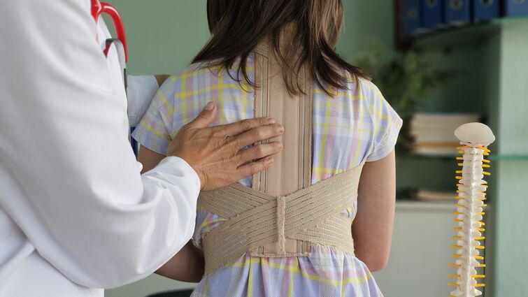 Doctor adjusts spine brace on young patient in a clinical setting, focusing on health and wellness
