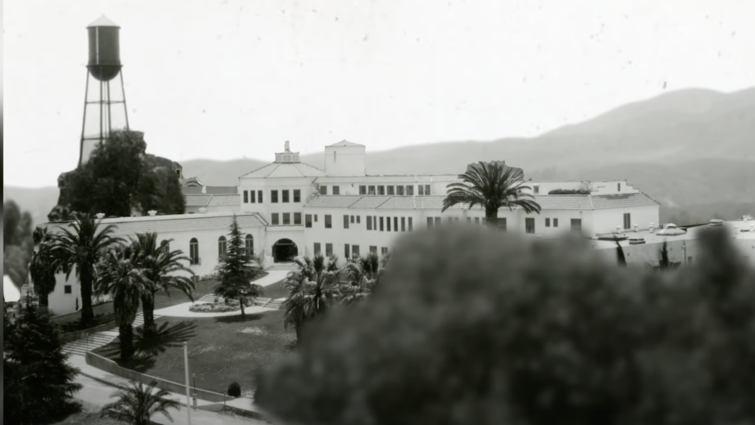 black and white photo of a university campus, hills in the background, trees in the foreground