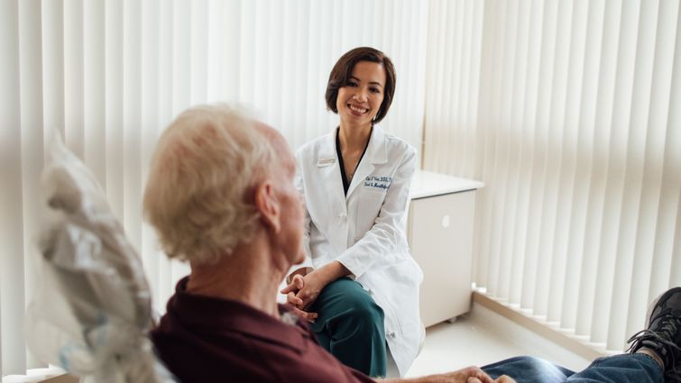 Asian female doctor sitting in a doctor's office with a male, white-haired man