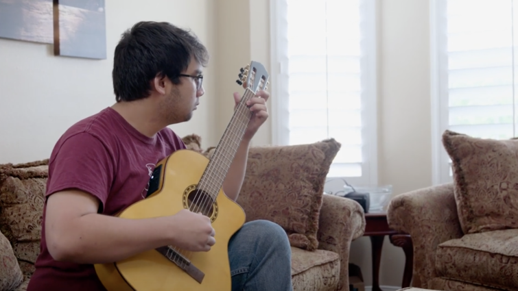 Tyler Rojanaroj sits on a couch playing guitar