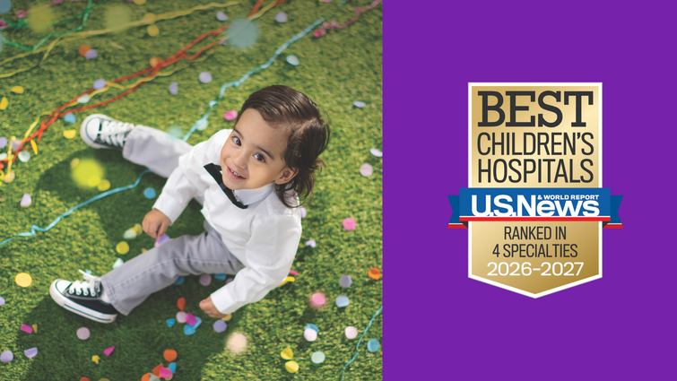 young boy smiles while sitting on grass with confetti, US News badge on purple background