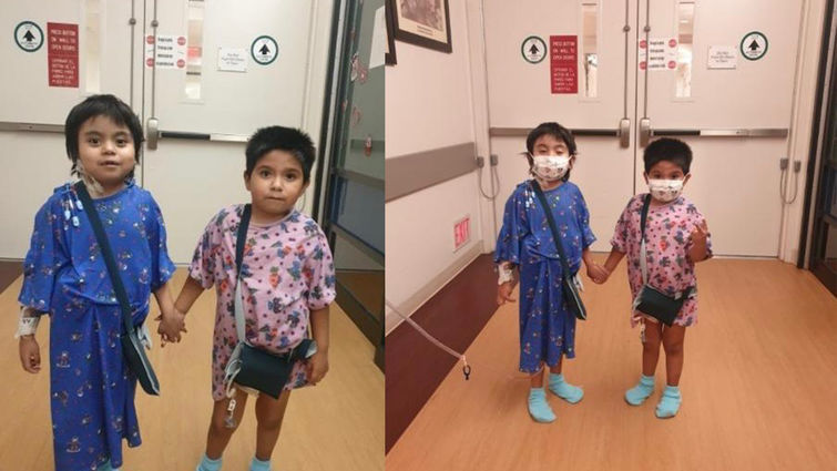 two young boys standing in hospital gowns holding hands