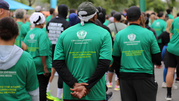 A large group of participants wearing green event shirts walk together along a street during the “Stand Up to Stigma” 5K. 