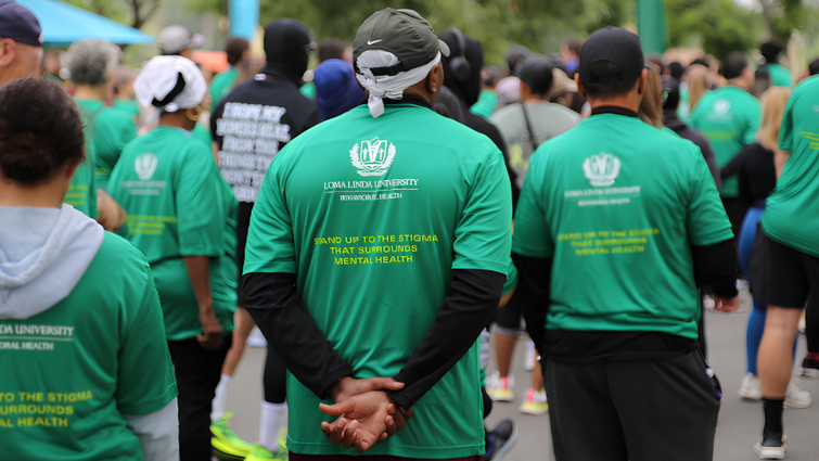 A large group of participants wearing green event shirts walk together along a street during the “Stand Up to Stigma” 5K. 