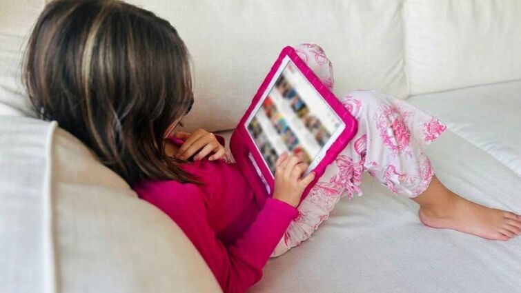 Girl watches videos on iPad while sitting on couch.
