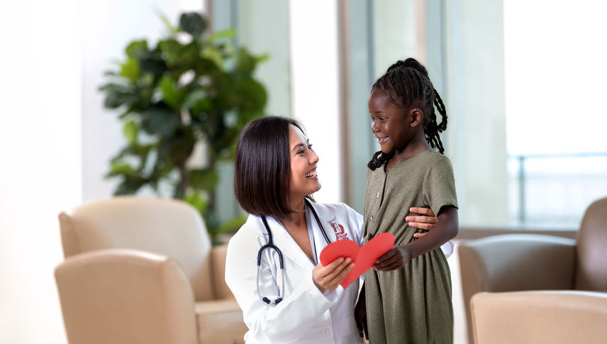 Female physician with young Black female holding a red paper heart