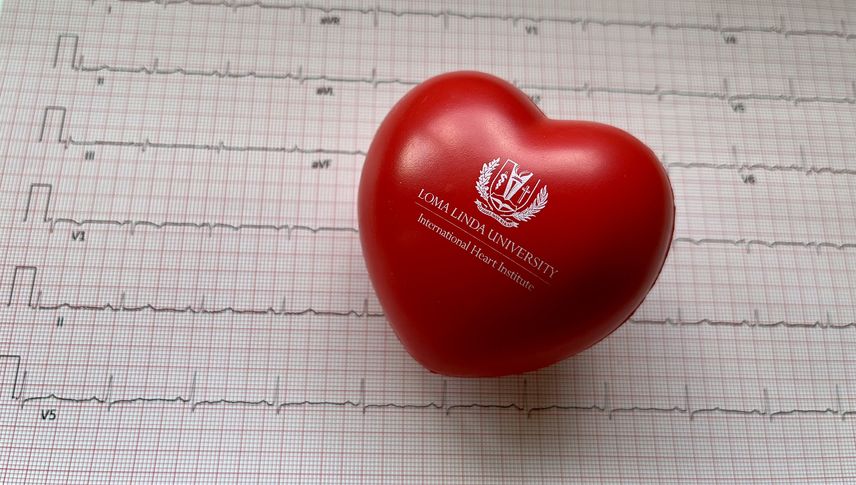 Red heart-shaped stressball against backdrop of ECG printout
