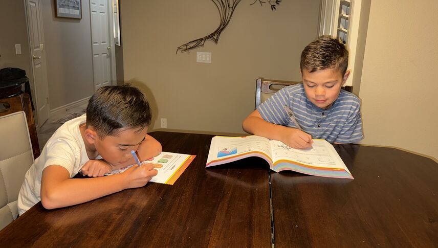 Two young boys sitting at a table working on work books