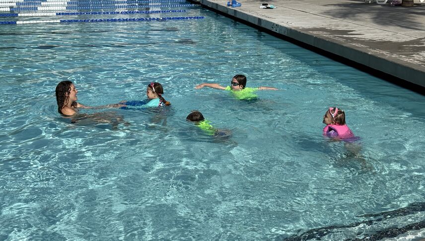 Four kids swimming towards swim instructor at the Drayson Center pool