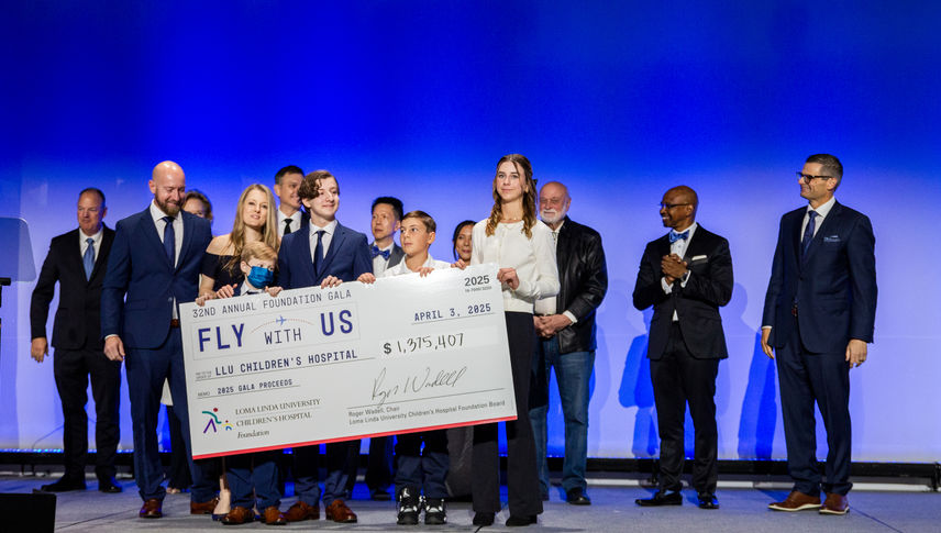 Hospital leadership, staff, and patient stand on stage holding large check with total number of funds raised at charity event