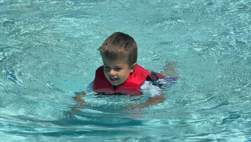 Young boy swims in pool with US Coast-guard approved life vest