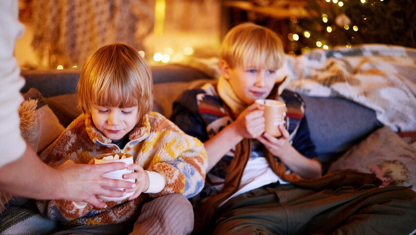Two young boys sitting on a couch drinking hot chocolate 