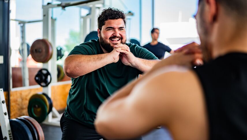 Mid adult man doing squats with personal trainer at gym
