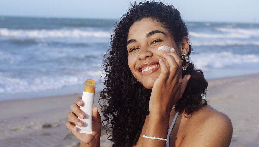 Young woman applying sunscreen on her face at the beach
